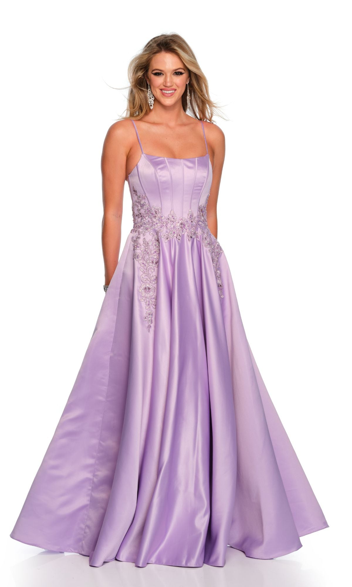 A woman wearing the Long Formal Dress 11338 by Dave and Johnny, a floor-length lavender satin A-line ball gown with thin straps and floral lace embellishments on the scoop bodice, stands and smiles.